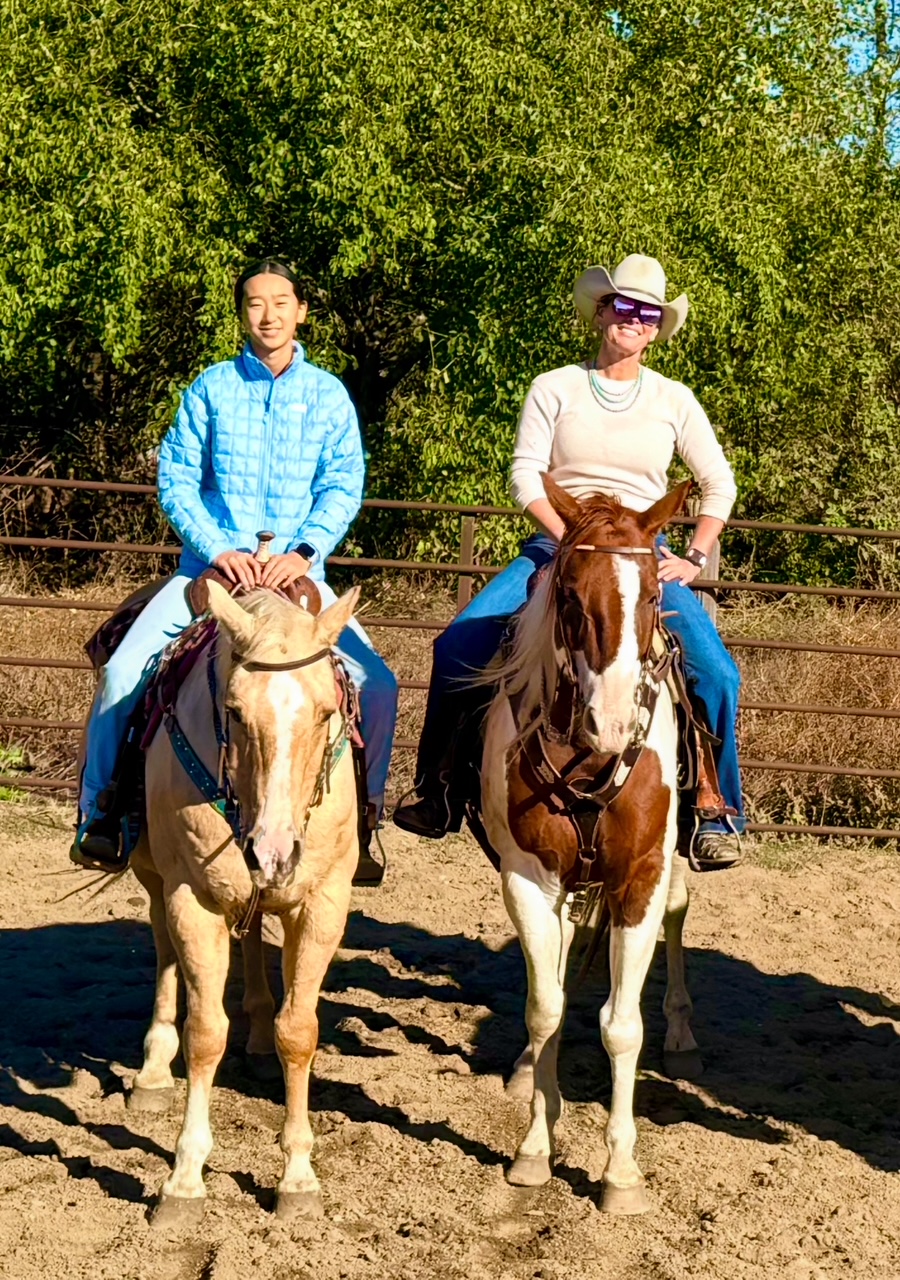 Addie and Stella riding horses in the arena